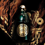 Refect Beauty Guerlain Oud Essentiel eau de parfum in a dark green glass bottle against a textured wood background