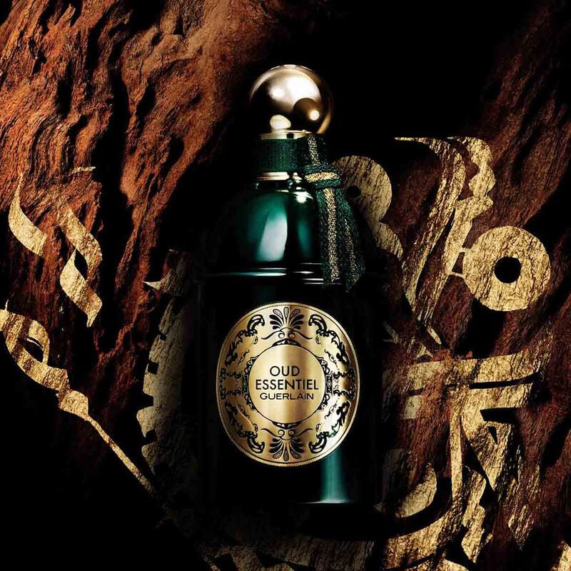Refect Beauty Guerlain Oud Essentiel eau de parfum in a dark green glass bottle against a textured wood background