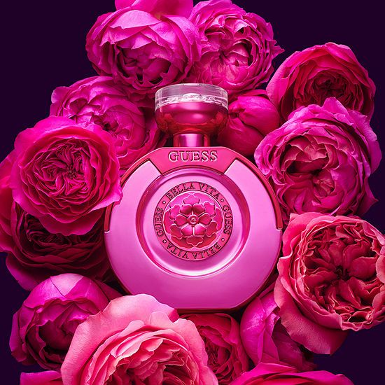 Refect Beauty Guess Bella Vita La Mia perfume bottle surrounded by vibrant pink roses on a dark background