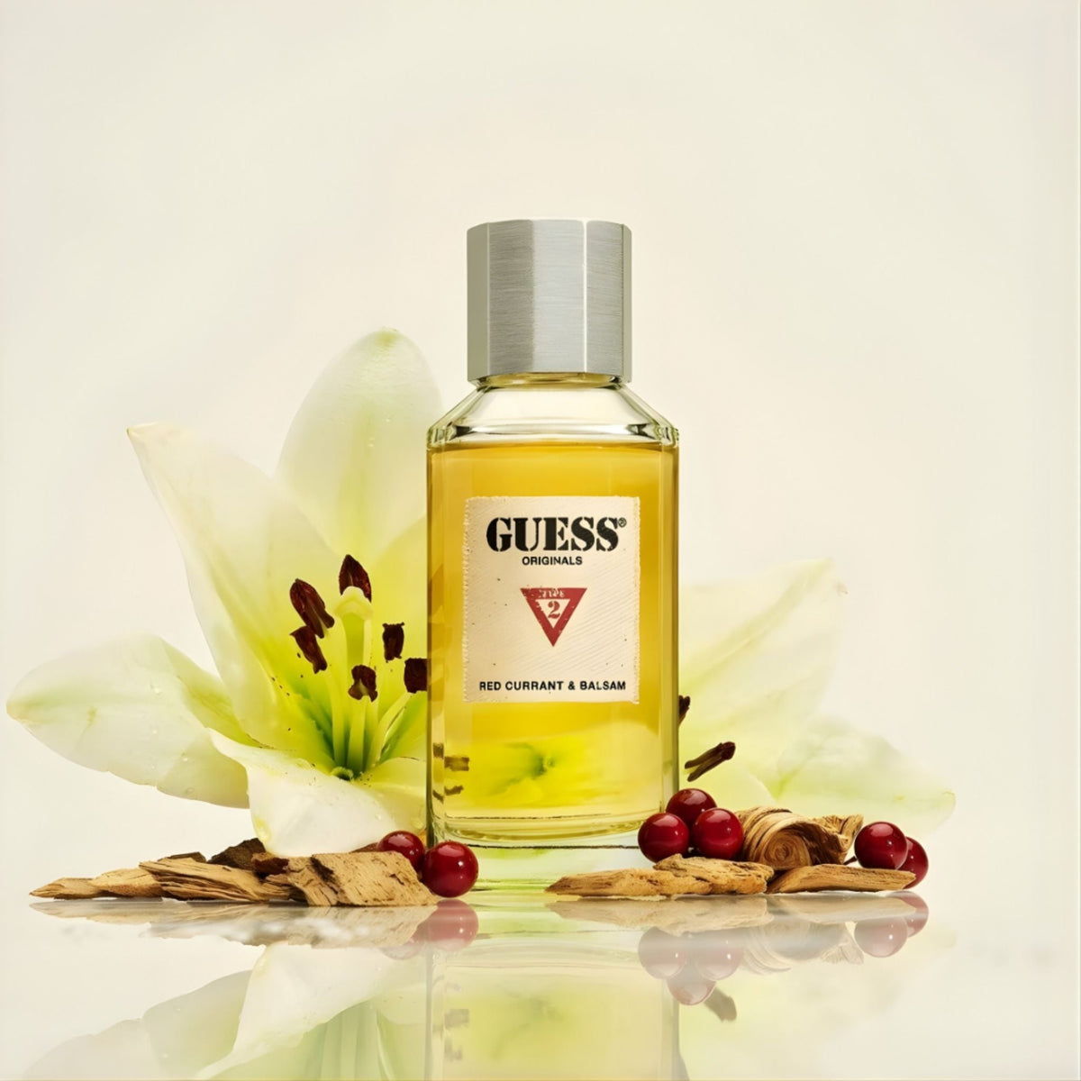 Refect Beauty Guess Red Currant & Balsam Eau De Parfum bottle surrounded by a white lily, red berries, and wood chips.
