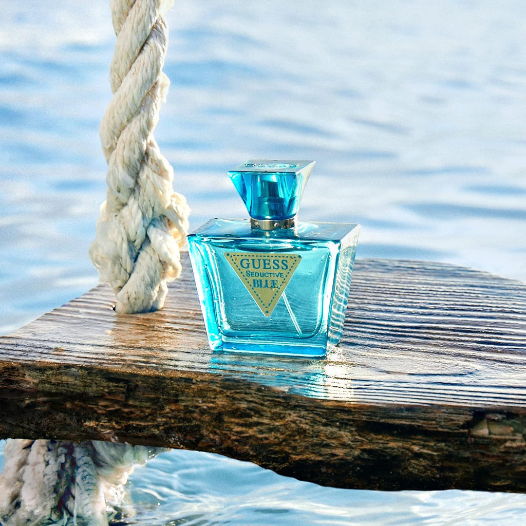 Refect Beauty Guess Seductive Blue Eau de Toilette bottle on a wooden platform over water with a fresh ocean backdrop