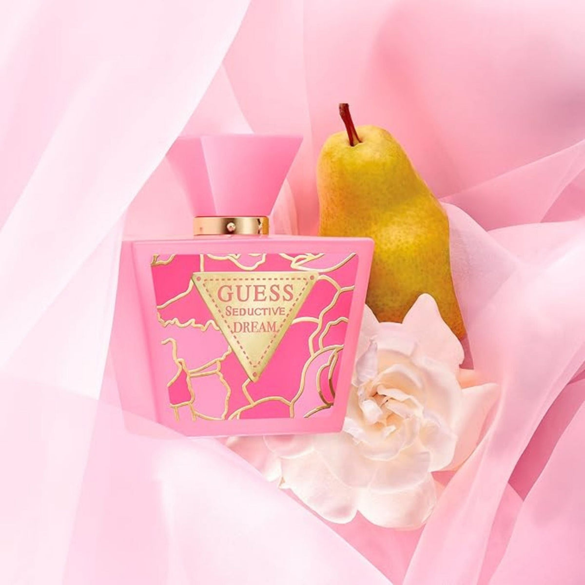 Refect Beauty Guess Seductive Dream perfume bottle with a fresh pear and white flower on a soft pink fabric background.