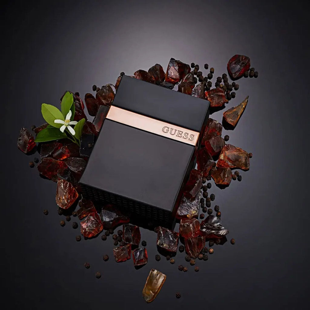 Refect Beauty Guess Seductive Homme Noir fragrance bottle surrounded by black pepper, amber stones, and orange blossoms.