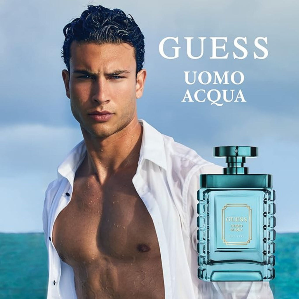 Refect Beauty Guess Uomo Acqua fragrance bottle next to a shirtless man on a beach, representing a fresh aquatic scent.