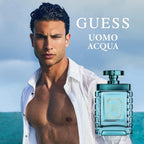 Refect Beauty Guess Uomo Acqua fragrance bottle next to a shirtless man on a beach, representing a fresh aquatic scent.