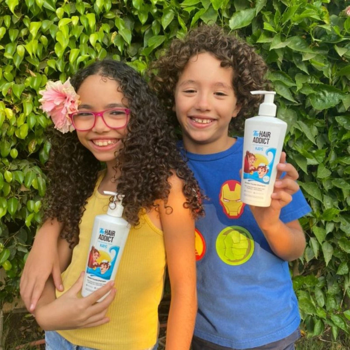 Refect Beauty Hair Addict Bubble Trouble conditioner bottles held by two smiling children with curly hair outdoors