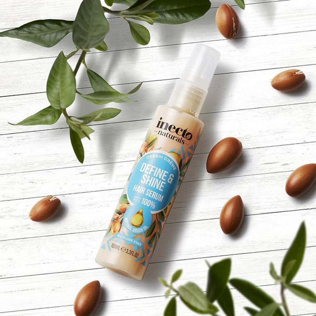 Refect Beauty Inecto Naturals Argan Oil hair serum bottle with argan nuts and green leaves on a white wooden surface.