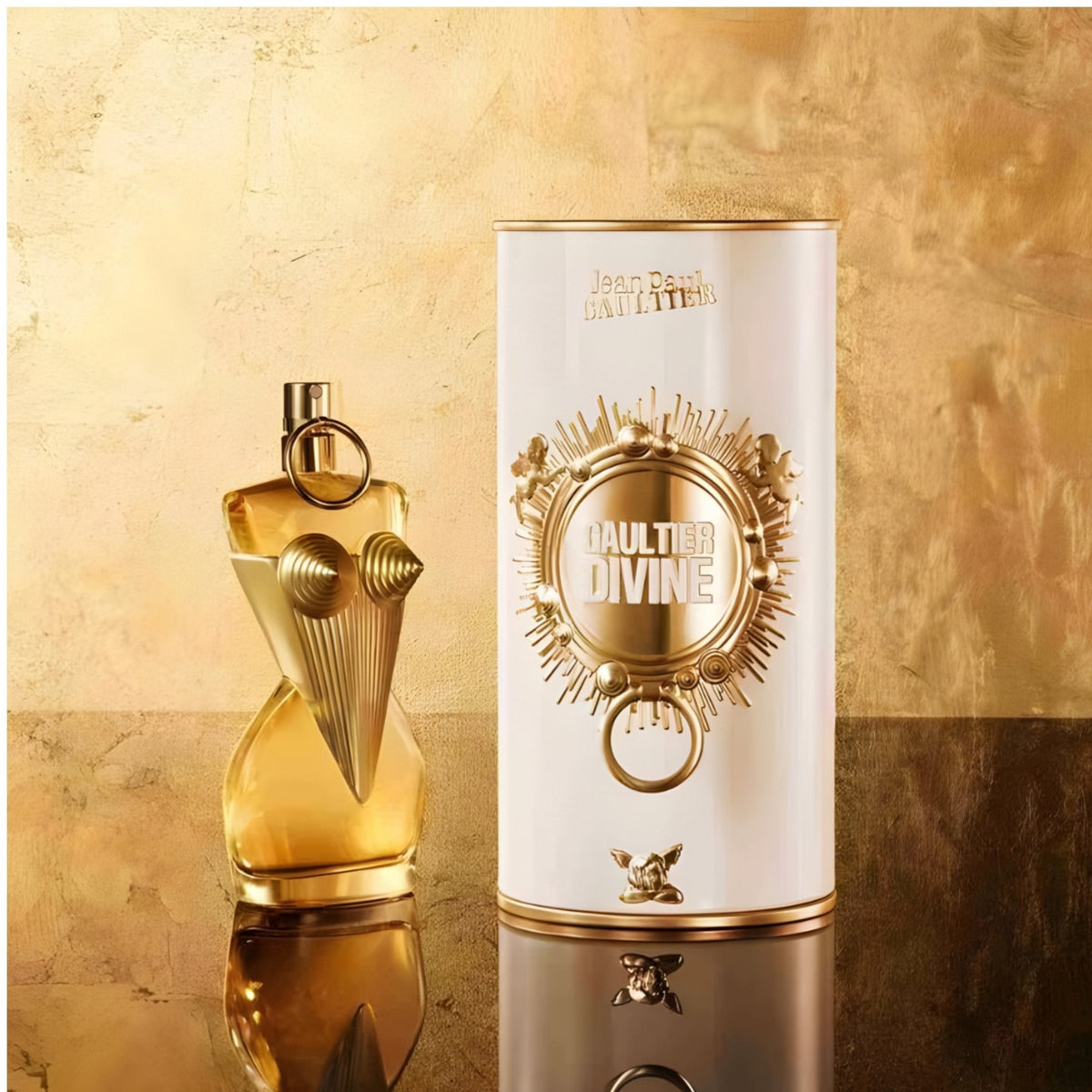 Refect Beauty Jean Paul Gaultier Divine Eau de Parfum bottle and white cylindrical gift tin on a gold reflective surface