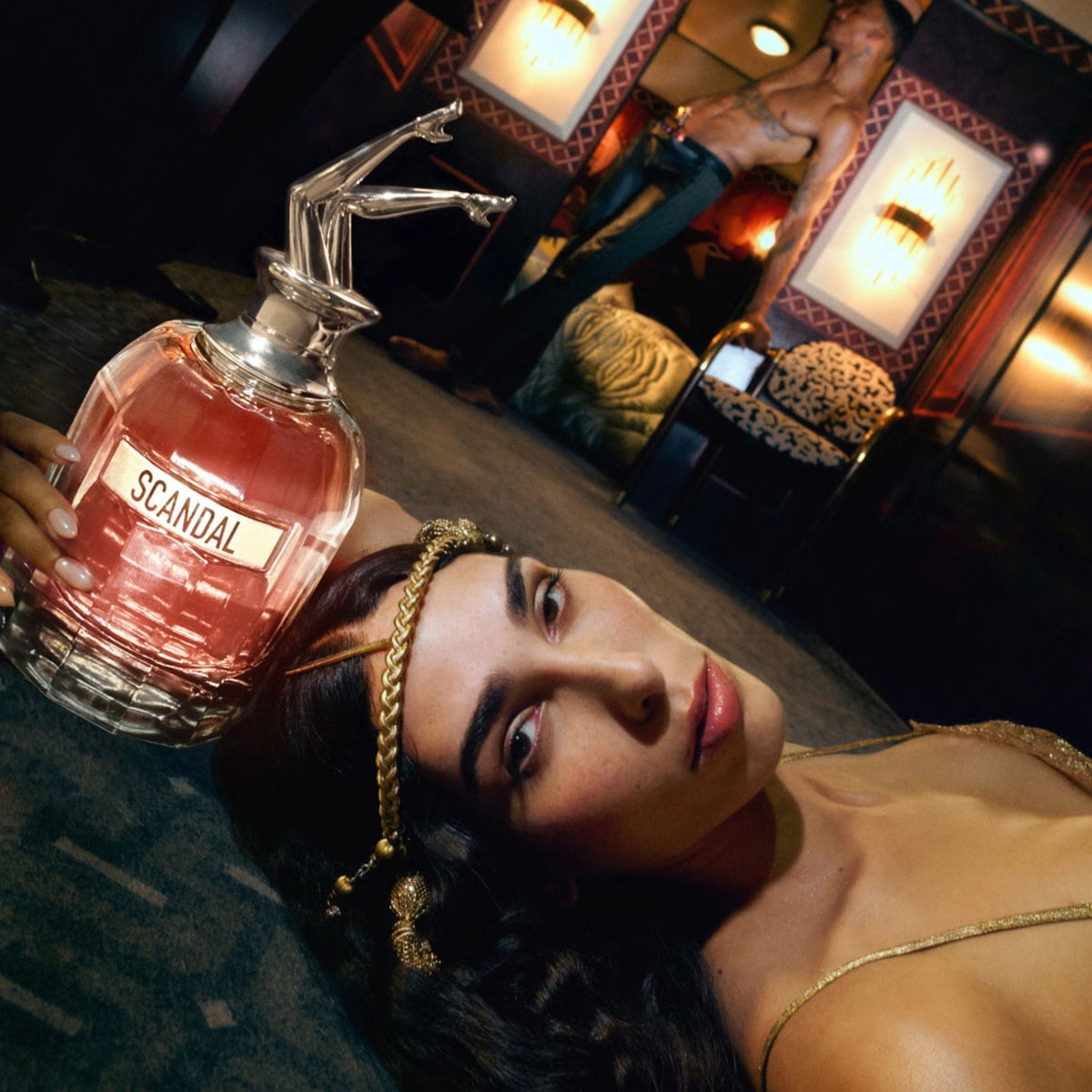 Refect Beauty Jean Paul Gaultier Scandal perfume bottle with iconic legs cap held by a woman in a glamorous setting