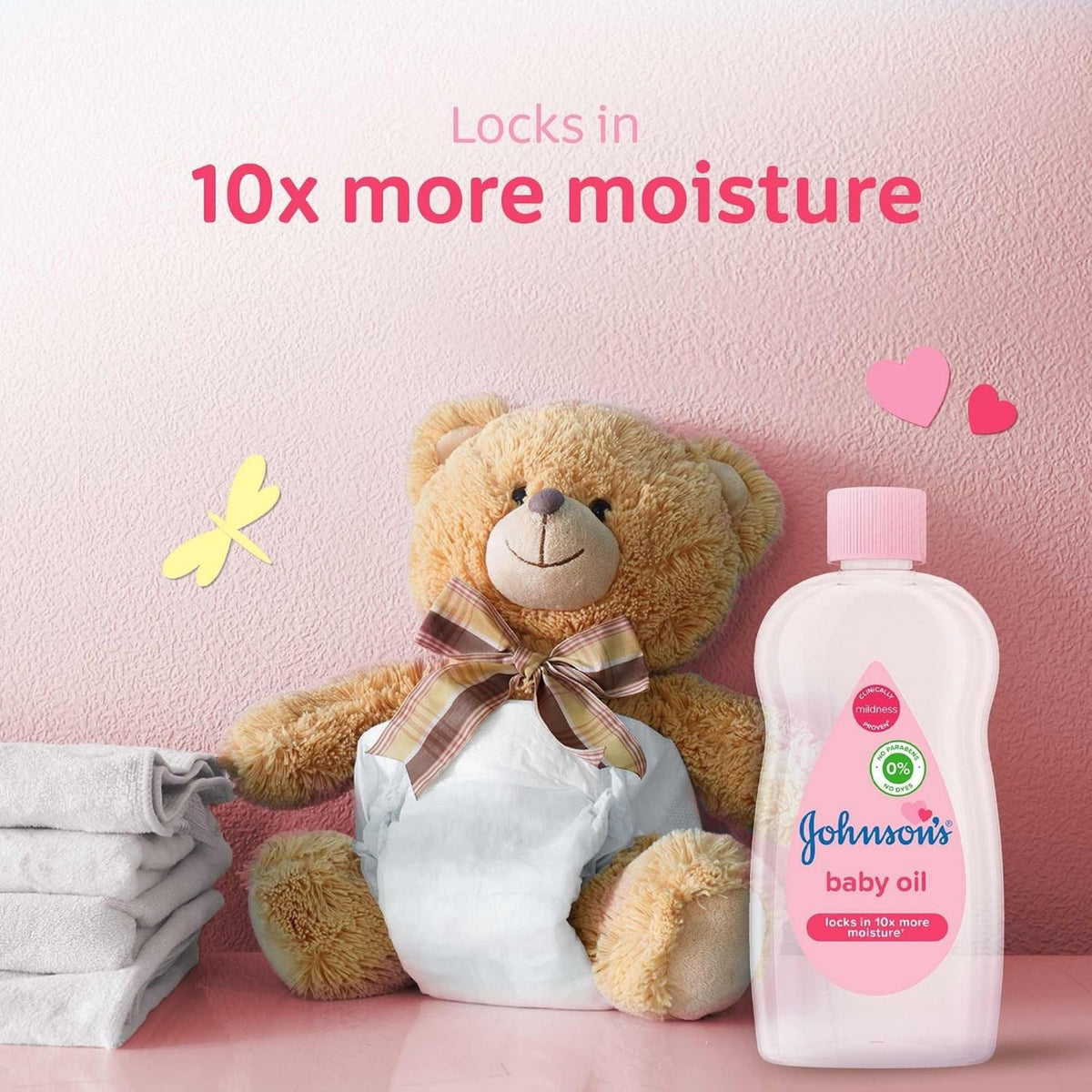 Refect Beauty Johnson's Baby Oil bottle next to a teddy bear on a pink background, promoting 10x moisture retention.