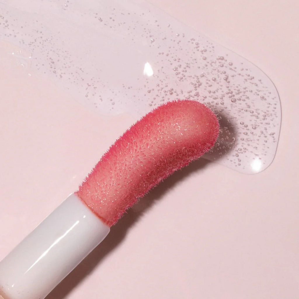 Refect Beauty Astra Pure Beauty Juicy Lip Oil applicator with a clear, hydrating lip gloss texture on a pink surface