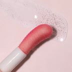Refect Beauty Astra Pure Beauty Juicy Lip Oil applicator with a clear, hydrating lip gloss texture on a pink surface