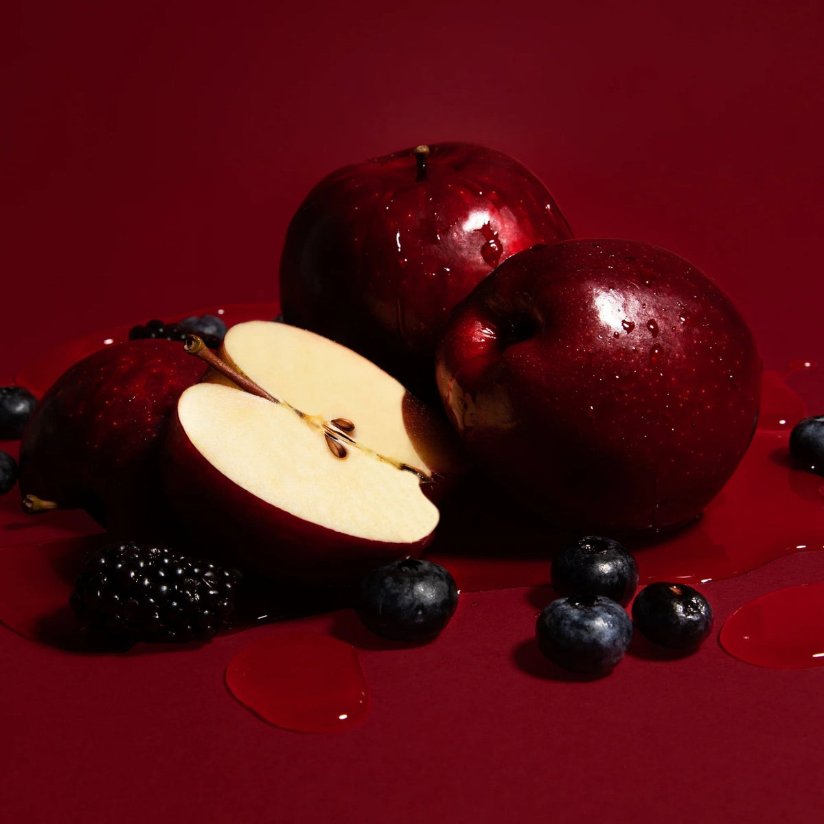 Refect Beauty Kayali Eden Juicy Apple perfume campaign featuring fresh red apples and berries on a deep red background.