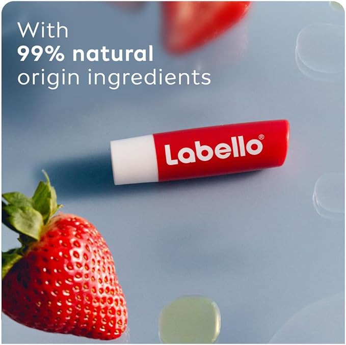 Refect Beauty Labello Strawberry Shine lip balm tube next to a fresh strawberry on a blue surface