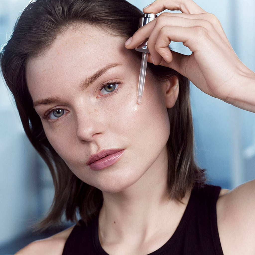 Refect Beauty model applying Lancôme Advanced Génifique youth activating serum with a glass dropper to her cheek