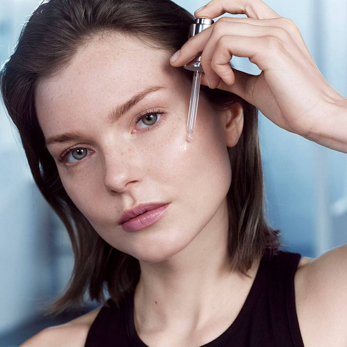 Refect Beauty model applying Lancôme Advanced Génifique youth activating serum with a glass dropper to her cheek