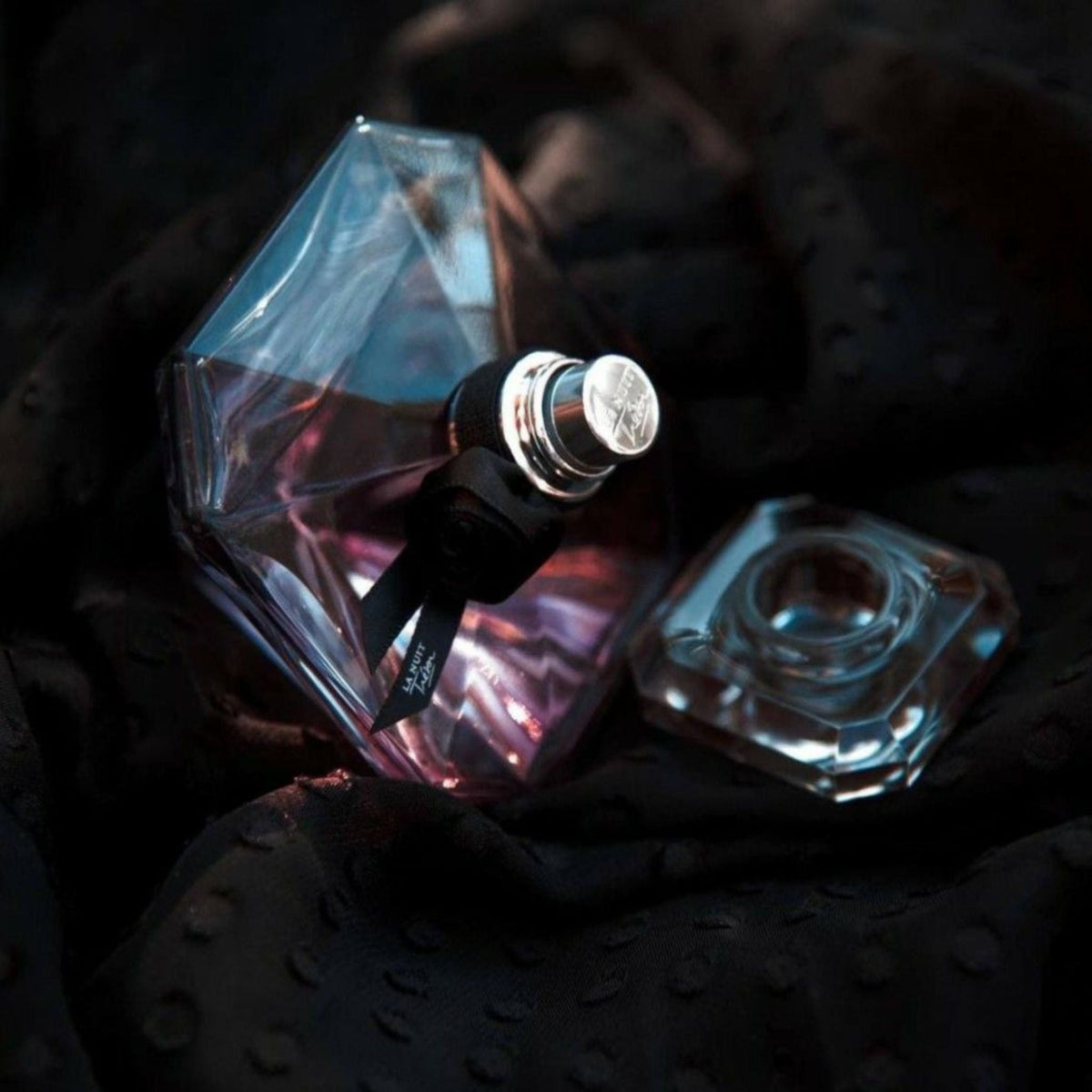 Refect Beauty Lancome La Nuit Tresor Eau de Parfum in a diamond-shaped glass bottle with a black ribbon on dark fabric