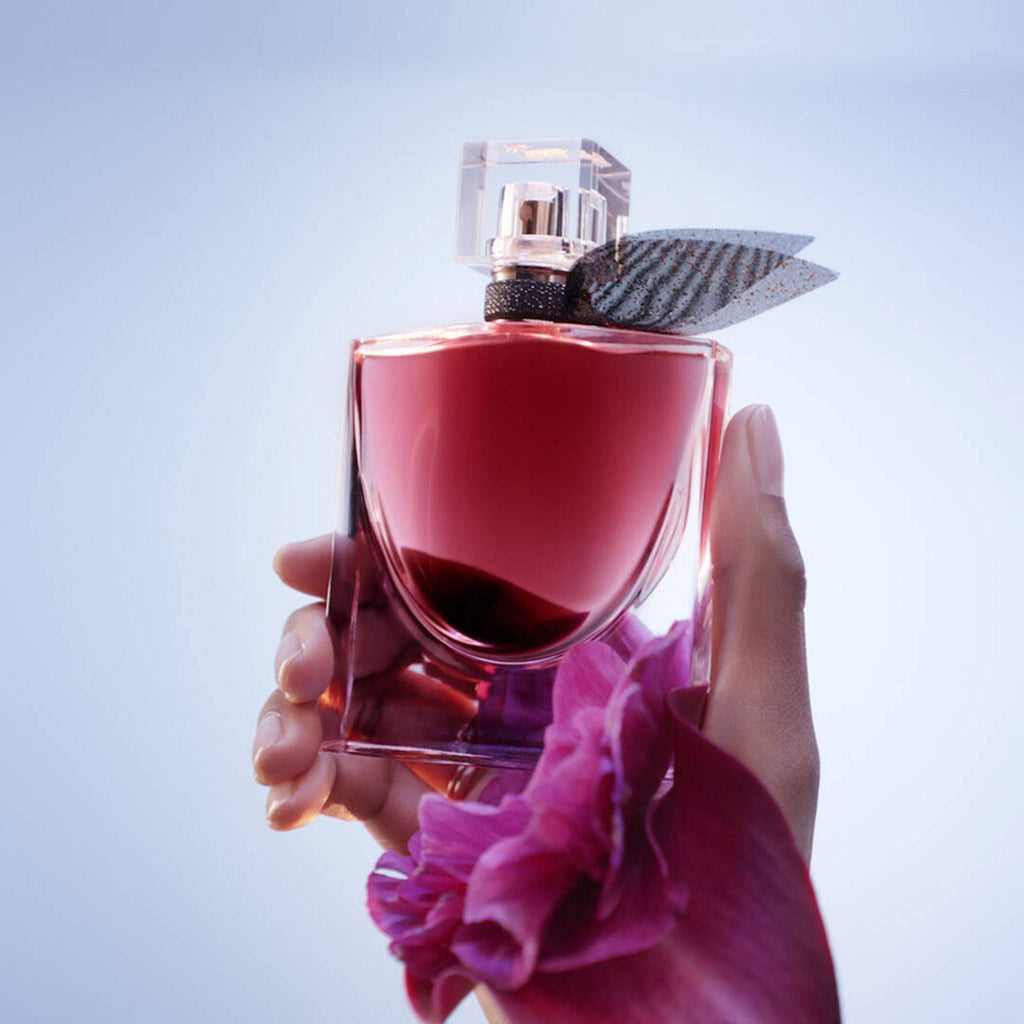Refect Beauty Lancome La Vie Est Belle L'Elixir perfume bottle held in hand with a purple flower against light background