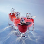 Refect Beauty Lancome La Vie Est Belle L'Elixir perfume bottles in varying shades of red on a blue reflective surface