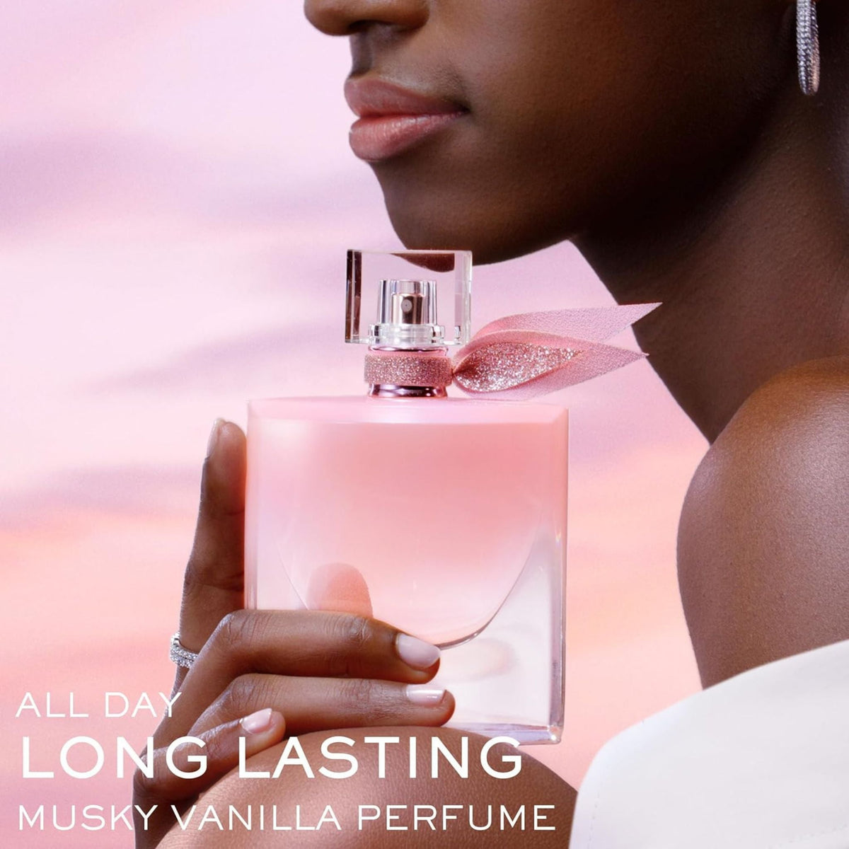 Refect Beauty Lancôme La Vie Est Belle Vanille Nude perfume bottle held by a woman against a soft pink sunset sky