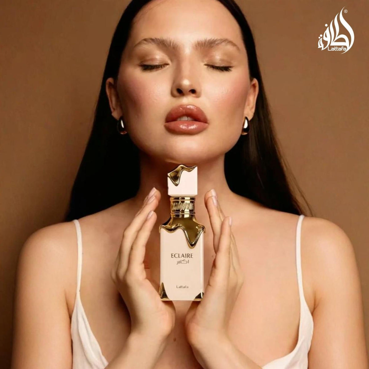 Refect Beauty Lattafa Eclaire perfume bottle held by a woman with glossy lips against a warm brown background