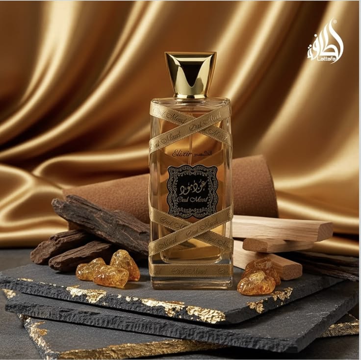 Refect Beauty Lattafa Oud Mood Elixir perfume bottle with gold ribbon on a slate base with oud wood and amber resin