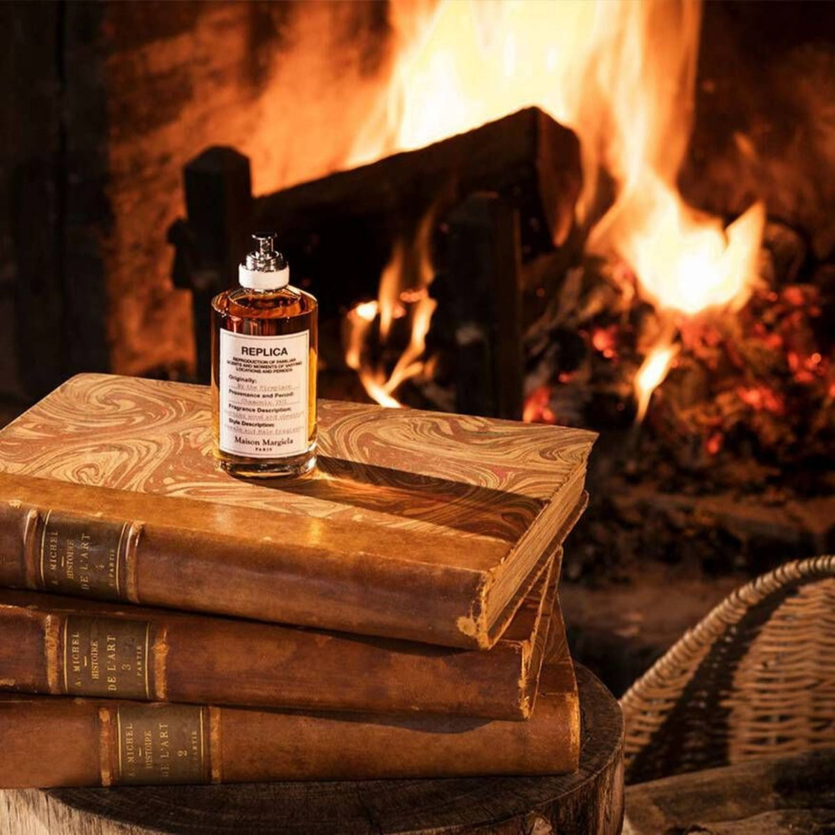 Refect Beauty Maison Margiela Replica By the Fireplace perfume bottle resting on vintage books before a warm fire.