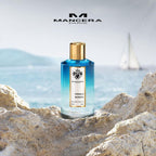 Refect Beauty Mancera French Riviera Eau de Parfum bottle with blue gradient glass on a rocky beach by the sea