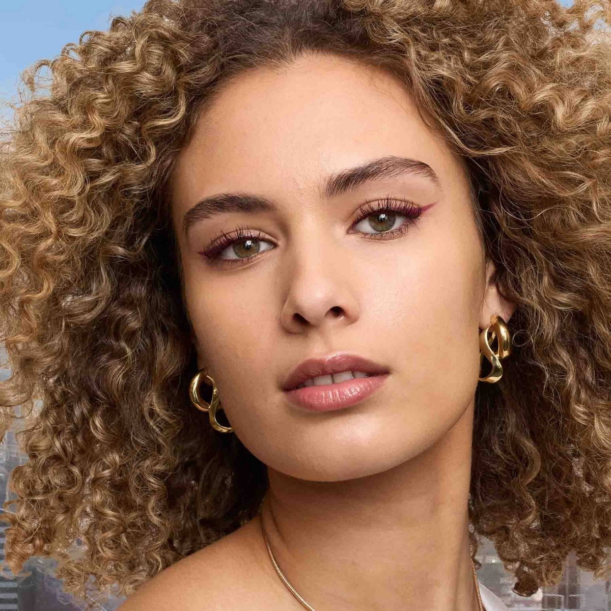 Refect Beauty model with curly hair wearing Maybelline Lash Sensational Sky High mascara for long, voluminous lashes.