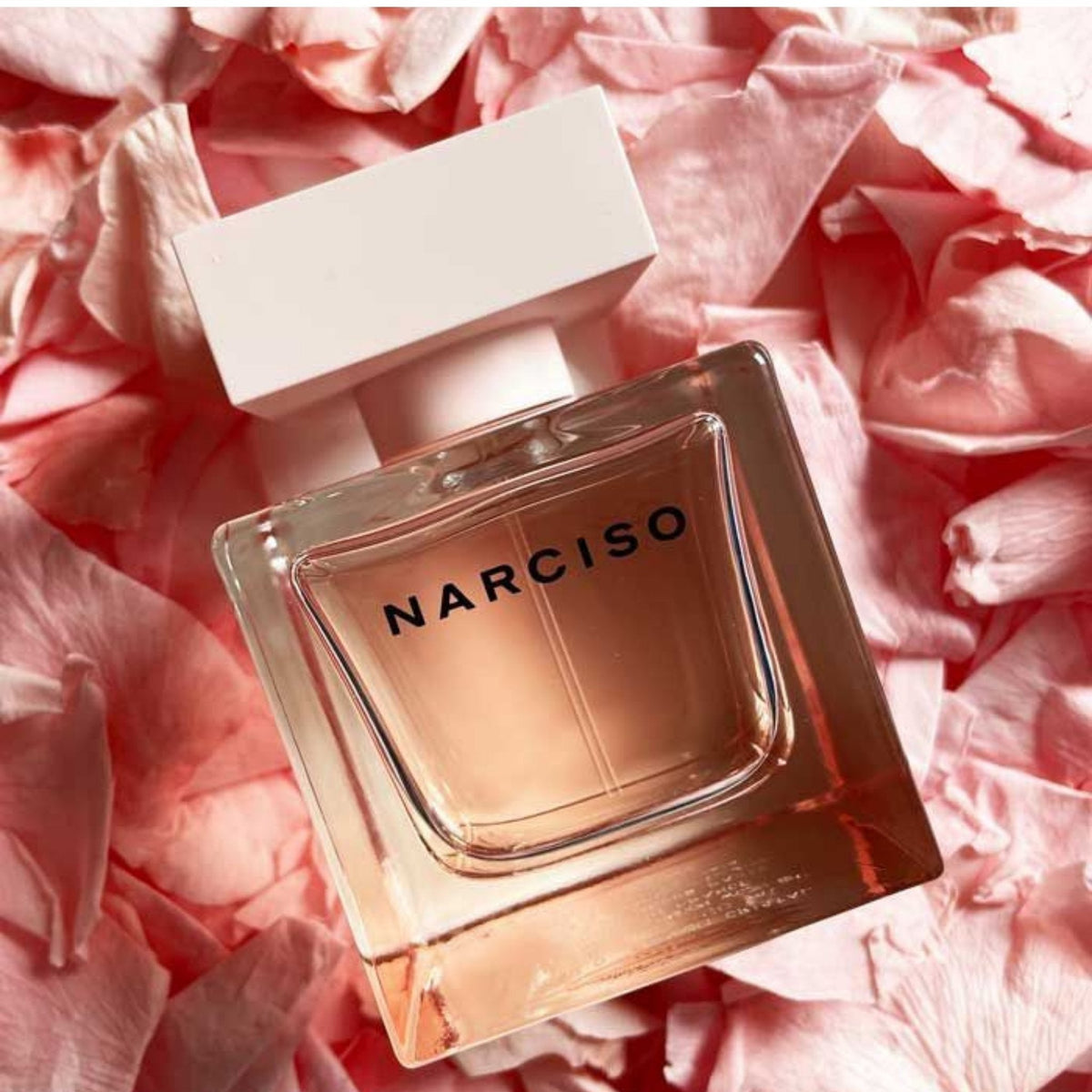 Refect Beauty Narciso Rodriguez Cristal Eau de Parfum bottle resting on a bed of soft pink flower petals.