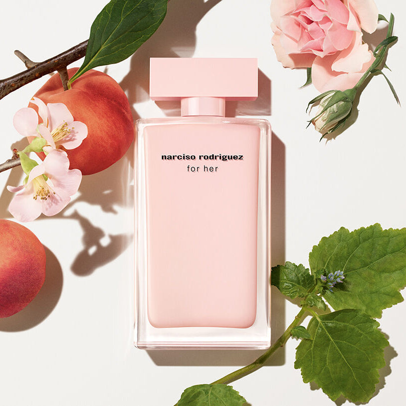 Refect Beauty Narciso Rodriguez For Her Eau de Parfum in a soft pink bottle surrounded by fresh roses and peaches.