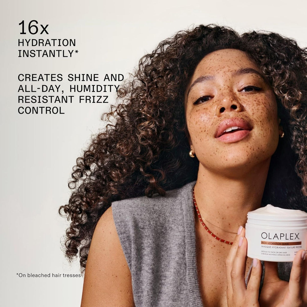 Refect Beauty model with curly hair holding an Olaplex Rich Hydration Mask jar for dry and damaged hair treatment