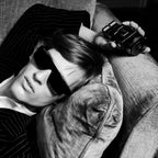 Refect Beauty model wearing sunglasses and a pinstripe suit, holding a Paco Rabanne Phantom Parfum bottle on a sofa.