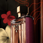 Refect Beauty Prada La Femme Intense Eau de Parfum bottle with deep red textured side and gold cap against floral art