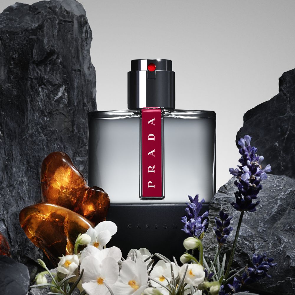 Refect Beauty Prada Luna Rossa Carbon Eau de Toilette bottle surrounded by dark rocks, lavender, and amber stones.