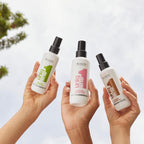 Refect Beauty presents three Revlon Uniq One leave-in hair treatment spray bottles held up against a bright sky.