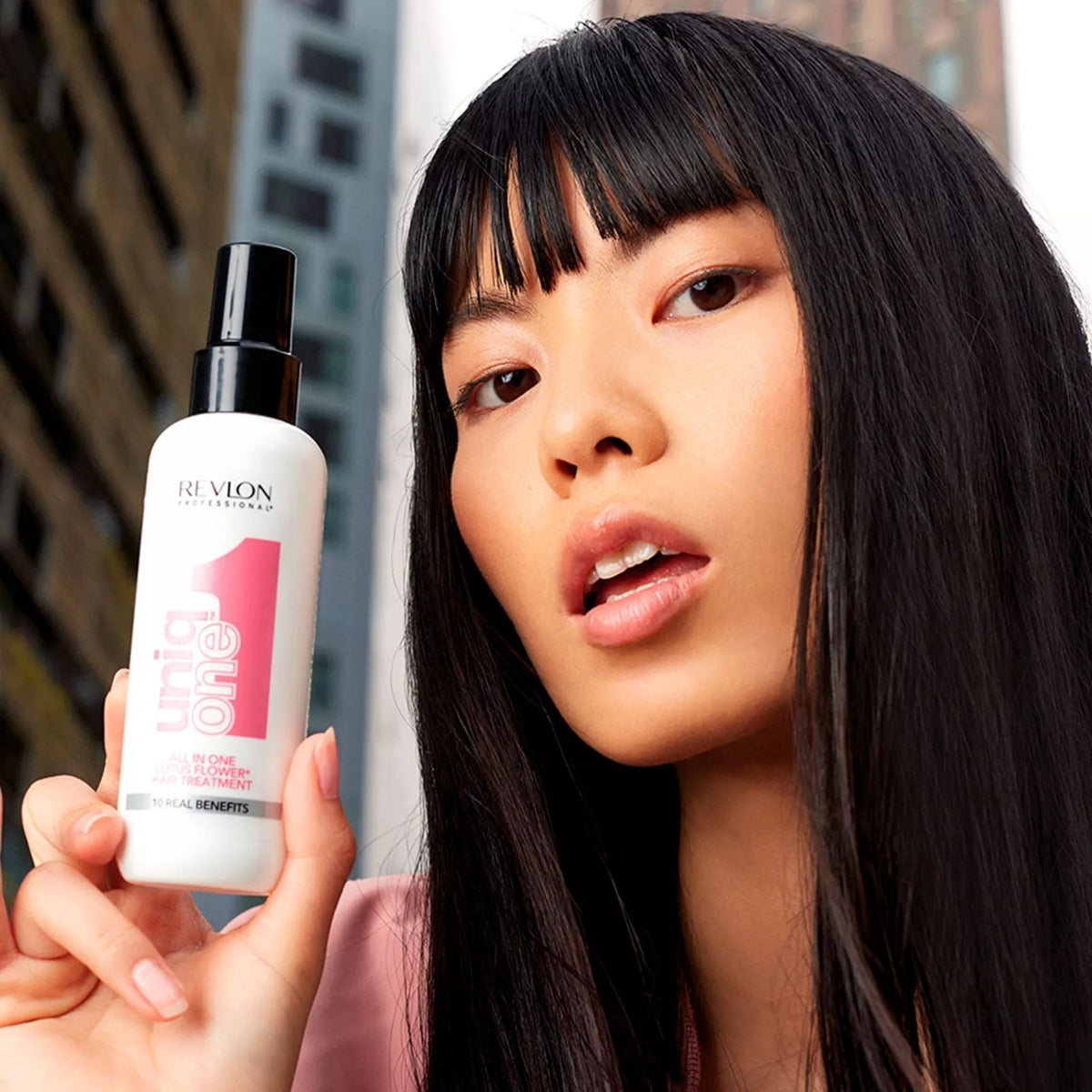 Refect Beauty model holding a bottle of Revlon Uniq One Lotus Flower leave-in hair treatment spray