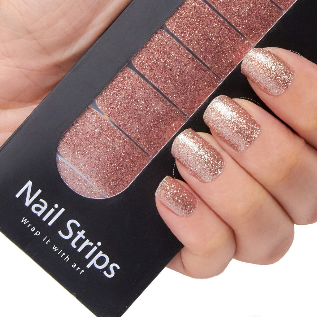 Refect Beauty Yolo nail strips with rose gold glitter finish applied to fingers, held against the product packaging.