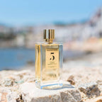 Refect Beauty Rosendo Mateu No. 5 Floral Amber perfume bottle on a stone surface with a blurred coastal background.