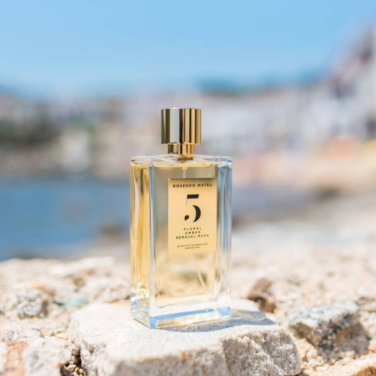 Refect Beauty Rosendo Mateu No. 5 Floral Amber perfume bottle on a stone surface with a blurred coastal background.