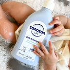 Refect Beauty Sanosan Baby Bath & Shampoo bottle held by a baby in a bubble bath, gentle 2-in-1 cleanser.
