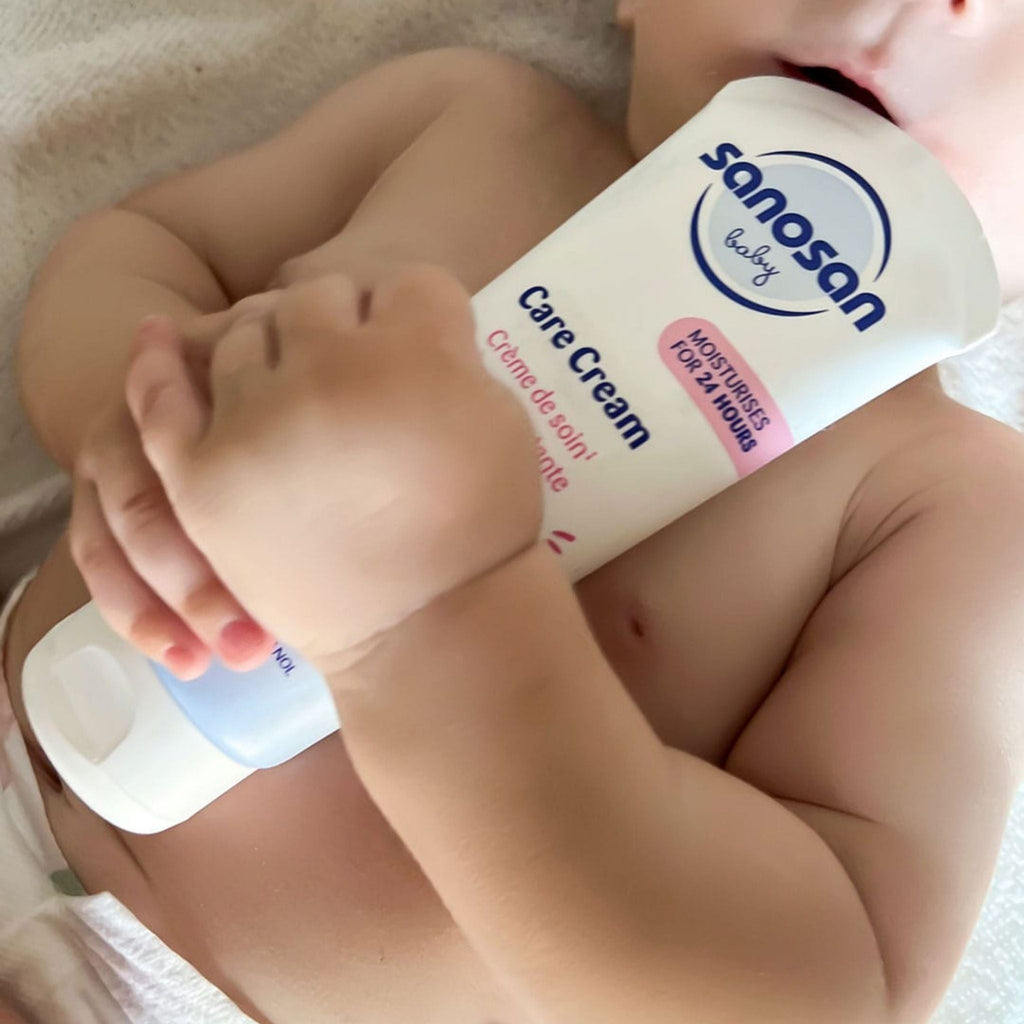 Refect Beauty Sanosan Baby Care Cream tube held by a baby, providing gentle 24-hour moisture for delicate skin.