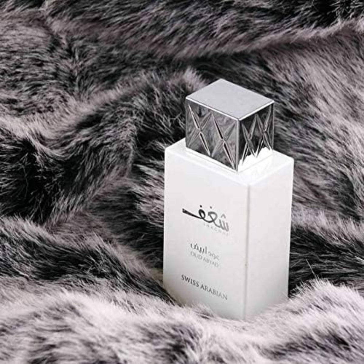 Refect Beauty Swiss Arabian Shaghaf Oud Abyad perfume bottle with a silver cap resting on a grey faux fur background.