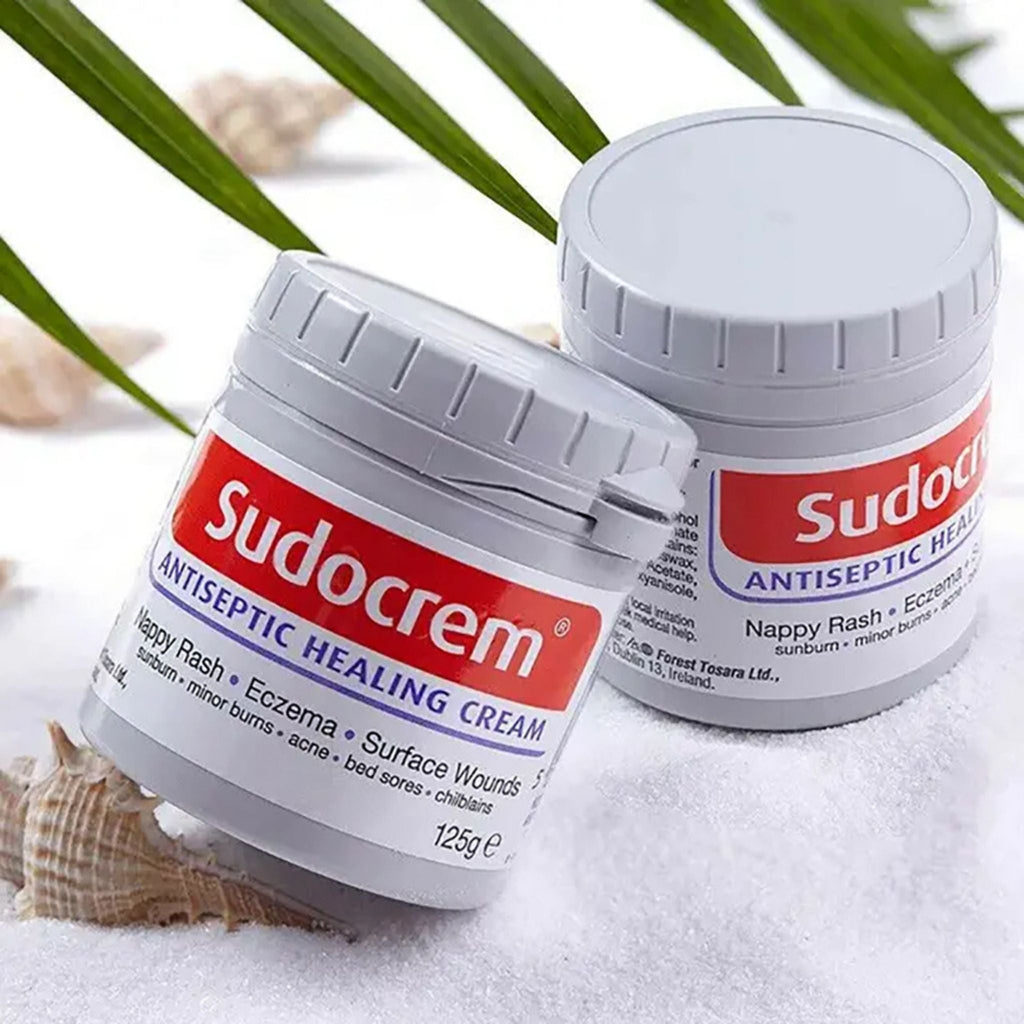 Refect Beauty Sudocrem antiseptic healing cream pots on white sand with palm leaves for minor skin irritation relief