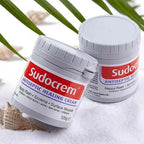 Refect Beauty Sudocrem antiseptic healing cream pots on white sand with palm leaves for minor skin irritation relief
