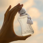 Refect Beauty Parfums de Marly Valaya Exclusif perfume bottle held in hand against a soft sunset sky background