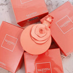 Refect Beauty Valentino Blush eau de parfum bottle with a rose-shaped cap surrounded by coral pink product boxes