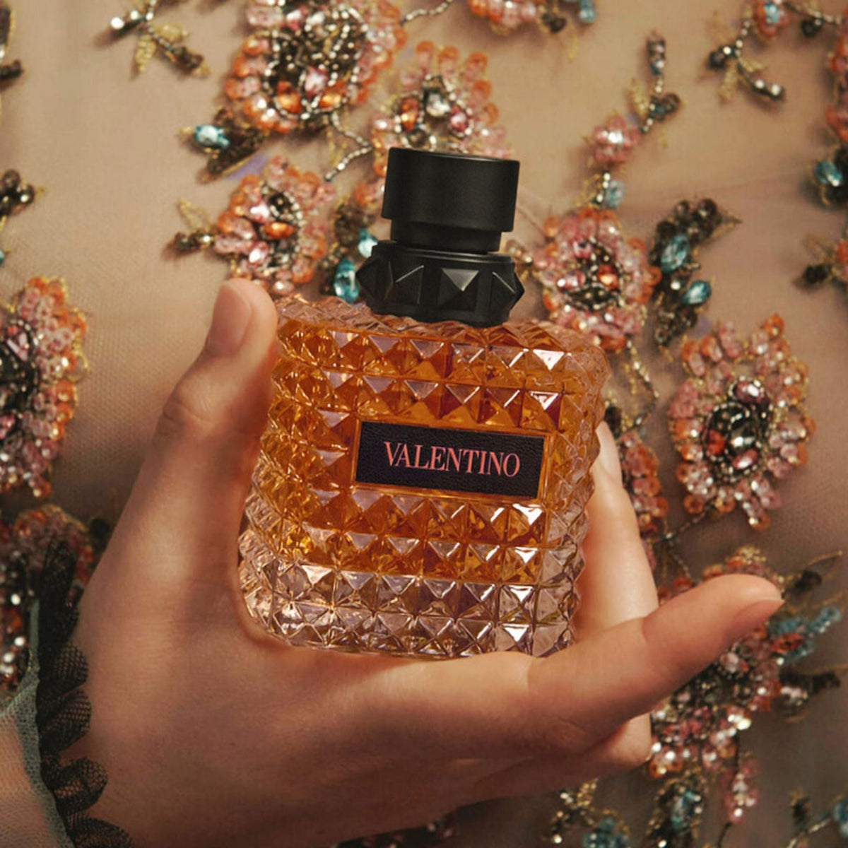 Refect Beauty Valentino Donna Born in Roma Coral Fantasy perfume bottle held in hand against a floral embroidered dress