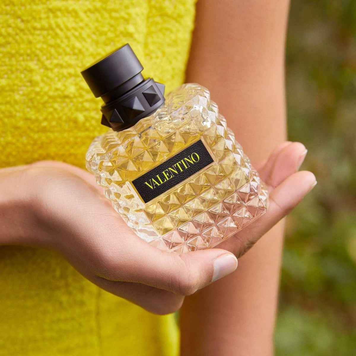 Refect Beauty Valentino Donna Born In Roma Yellow Dream perfume bottle held in a hand against a yellow textured background