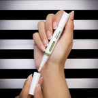 Refect Beauty Yolo Booster serum pen for nail and cuticle care held in a hand against a black and white striped background